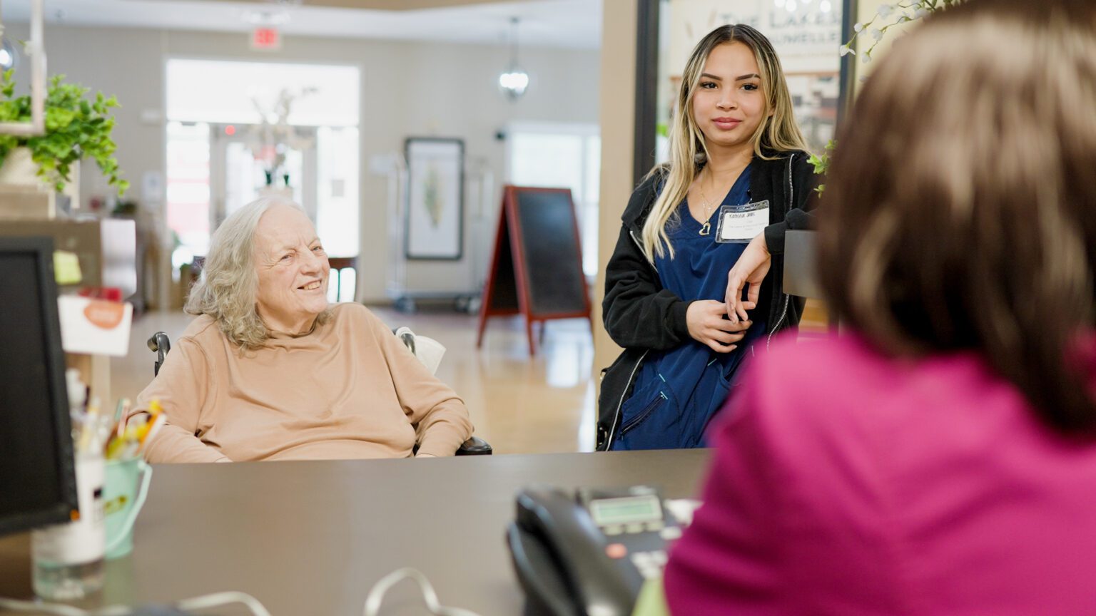two nurses talk to a resident at a skilled nursing facility